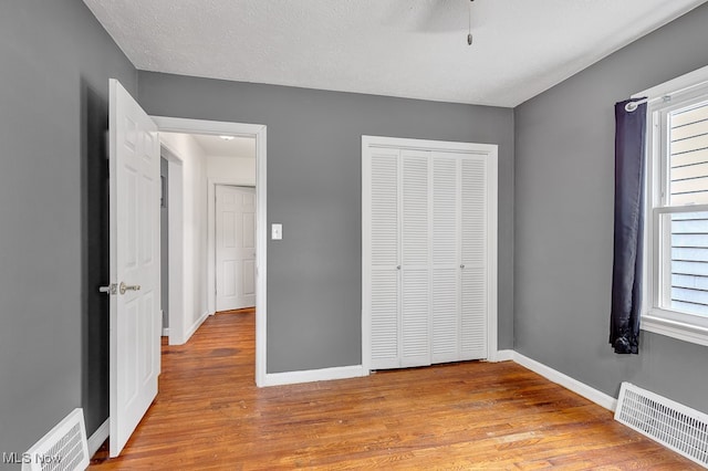 unfurnished bedroom featuring a closet, light hardwood / wood-style floors, multiple windows, and a textured ceiling