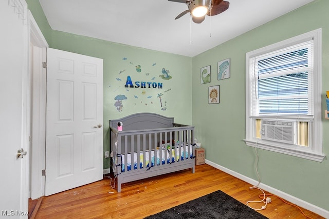 bedroom with a crib, hardwood / wood-style flooring, and ceiling fan