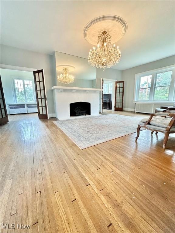 unfurnished living room featuring an inviting chandelier, a wealth of natural light, a high end fireplace, and wood-type flooring