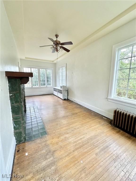 unfurnished living room featuring hardwood / wood-style flooring, a raised ceiling, a ceiling fan, radiator heating unit, and baseboards