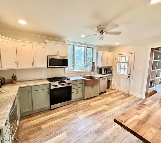 kitchen featuring light countertops, light wood-type flooring, a sink, a ceiling fan, and appliances with stainless steel finishes