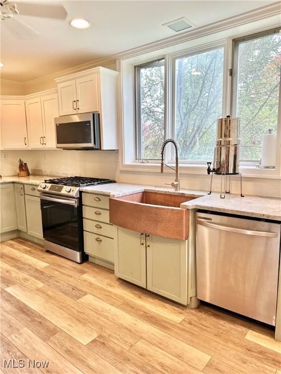 kitchen with white cabinets, a sink, stainless steel appliances, and light wood-style floors