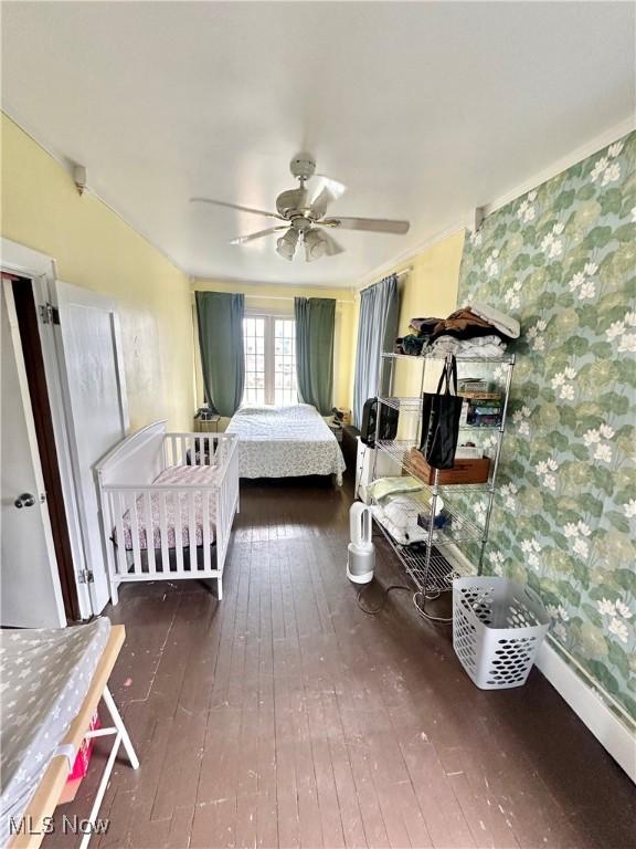 bedroom with baseboards, wallpapered walls, a ceiling fan, and wood-type flooring