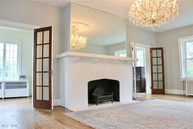 unfurnished living room with a notable chandelier, a fireplace with flush hearth, wood finished floors, radiator, and baseboards