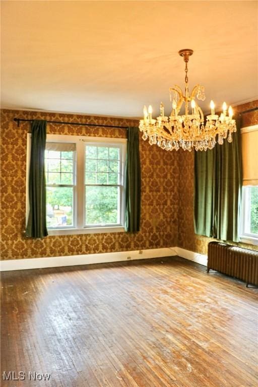 unfurnished room featuring hardwood / wood-style floors, baseboards, radiator heating unit, and a notable chandelier