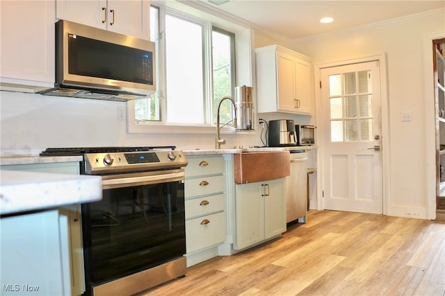 kitchen with ornamental molding, stainless steel appliances, white cabinets, and light wood-type flooring