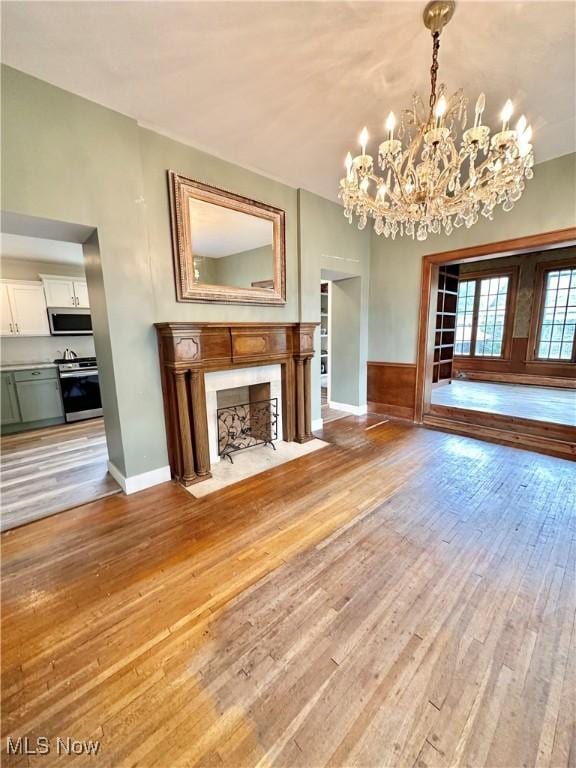 unfurnished living room with a notable chandelier, a fireplace, and light wood-type flooring