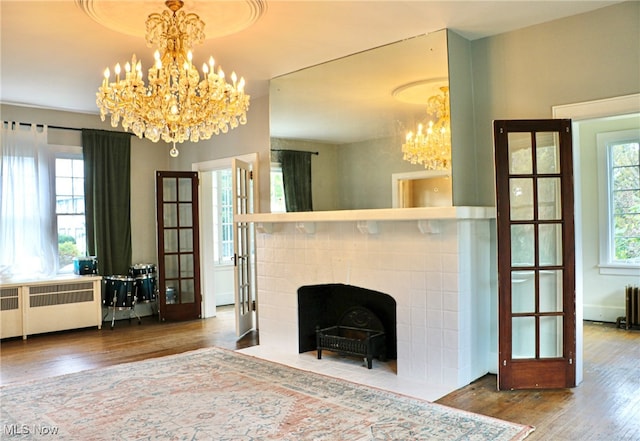 unfurnished living room featuring a tile fireplace, hardwood / wood-style flooring, radiator, and a notable chandelier