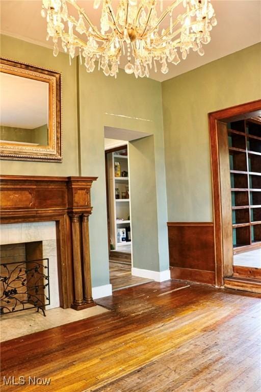 unfurnished living room featuring an inviting chandelier, hardwood / wood-style flooring, built in features, and a premium fireplace