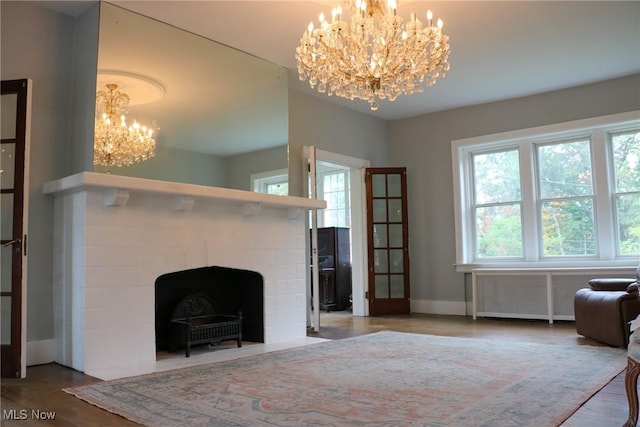 unfurnished living room with an inviting chandelier, radiator heating unit, baseboards, and wood finished floors