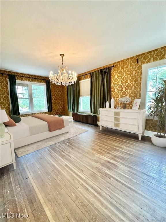 unfurnished bedroom featuring hardwood / wood-style floors, an inviting chandelier, wallpapered walls, multiple windows, and radiator heating unit