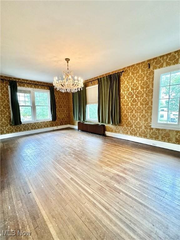 spare room featuring a notable chandelier, hardwood / wood-style flooring, radiator heating unit, baseboards, and wallpapered walls