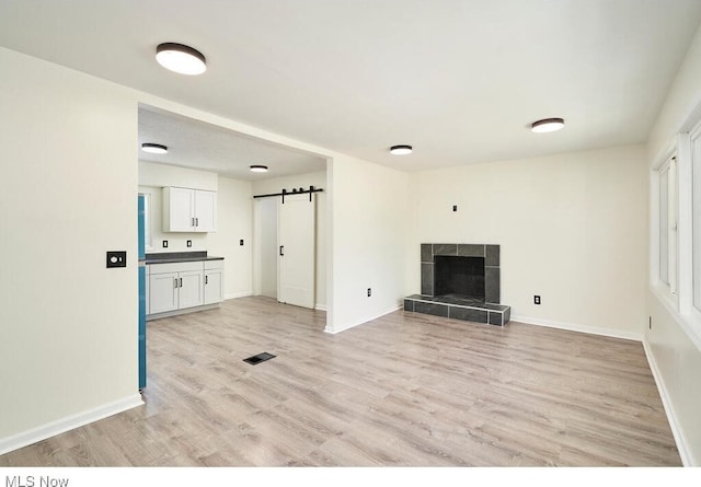 unfurnished living room featuring a barn door, a tile fireplace, and light hardwood / wood-style flooring