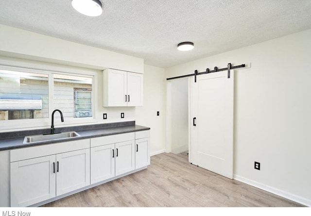 kitchen with light hardwood / wood-style floors, white cabinetry, a barn door, a textured ceiling, and sink