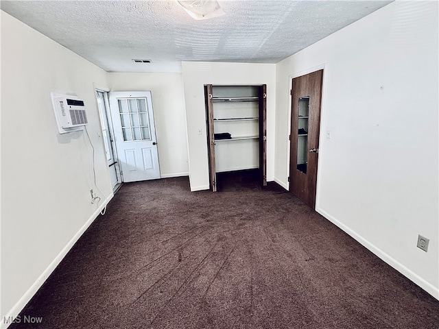 interior space with dark colored carpet, a textured ceiling, and an AC wall unit