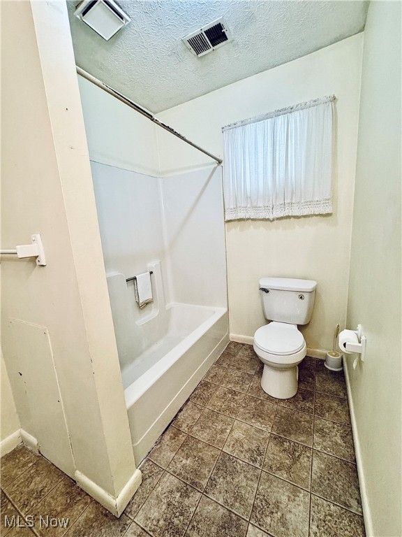 bathroom featuring tub / shower combination, a textured ceiling, and toilet