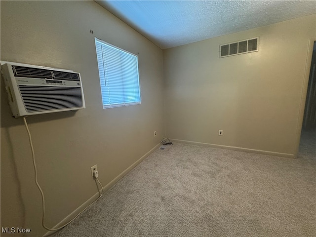 carpeted empty room featuring a wall mounted air conditioner and a textured ceiling