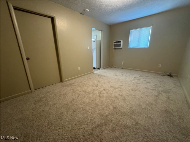 unfurnished bedroom featuring a textured ceiling, white refrigerator, light colored carpet, and an AC wall unit