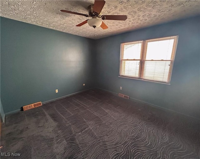 spare room featuring a textured ceiling, dark carpet, and ceiling fan