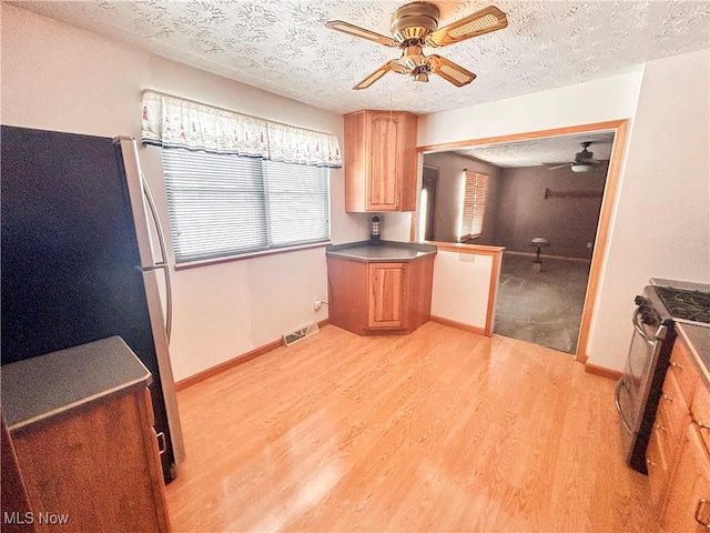 kitchen featuring ceiling fan, a textured ceiling, appliances with stainless steel finishes, and light hardwood / wood-style flooring