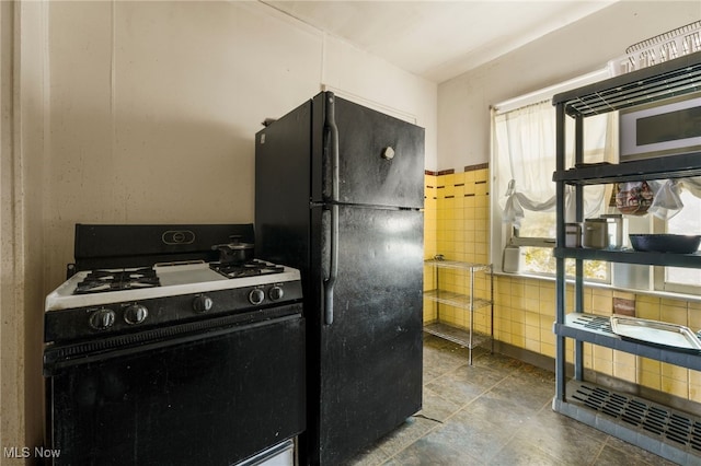 kitchen with tile walls, freestanding refrigerator, and range with gas stovetop