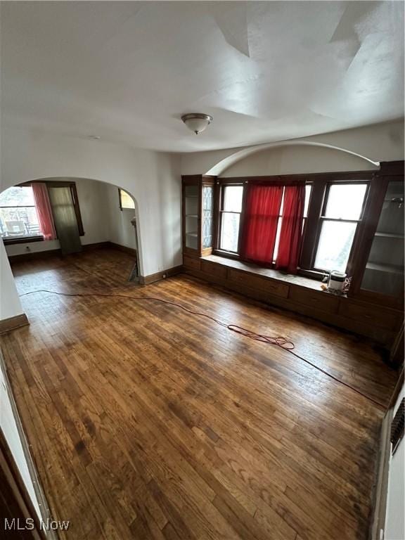 unfurnished room with arched walkways, plenty of natural light, dark wood-style floors, and baseboards