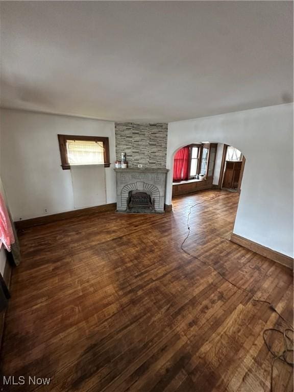 unfurnished living room featuring plenty of natural light, dark wood-style flooring, a fireplace, and arched walkways