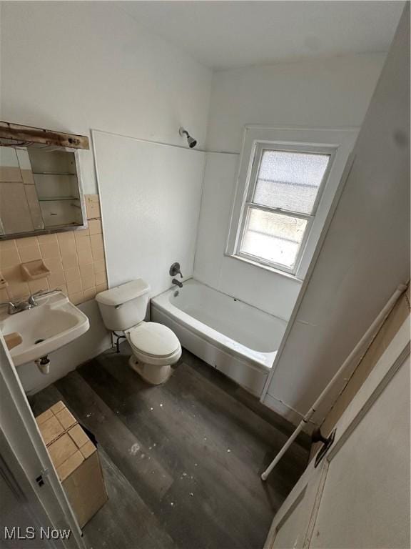 bathroom featuring toilet, wood finished floors,  shower combination, a sink, and tile walls