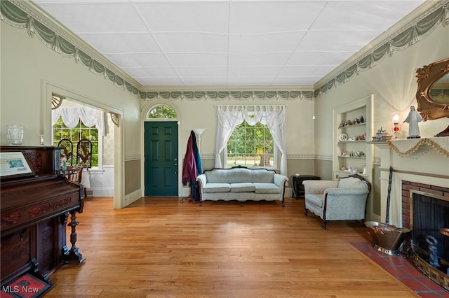 living area with crown molding, light wood-type flooring, built in features, and a fireplace