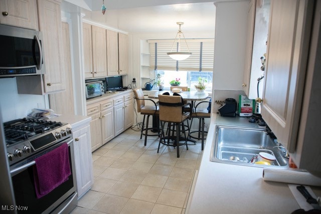 kitchen with light tile patterned flooring, stainless steel appliances, decorative light fixtures, and sink