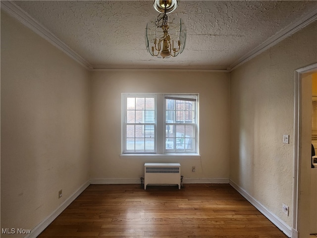 empty room featuring radiator heating unit, a textured ceiling, wood-type flooring, an inviting chandelier, and ornamental molding