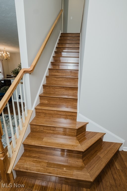 staircase with a notable chandelier and wood-type flooring