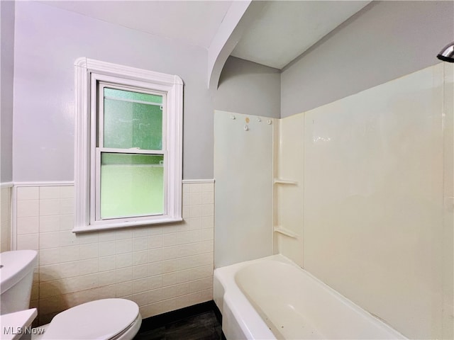 bathroom with tile walls, bathing tub / shower combination, hardwood / wood-style floors, and toilet