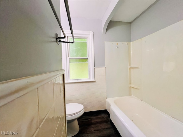 bathroom with tile walls, bathing tub / shower combination, hardwood / wood-style floors, and toilet