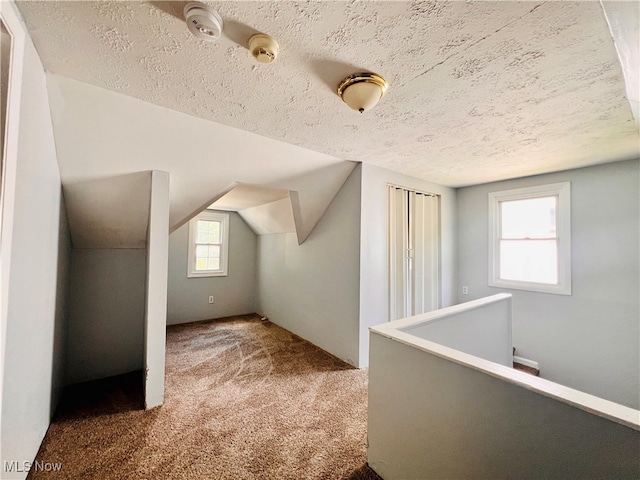 bonus room featuring a textured ceiling, a healthy amount of sunlight, carpet flooring, and vaulted ceiling