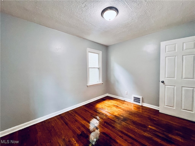 empty room with a textured ceiling and dark wood-type flooring