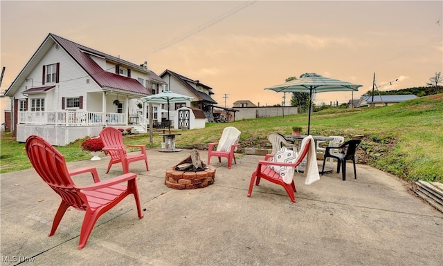 patio terrace at dusk with a storage shed, an outdoor fire pit, and a yard