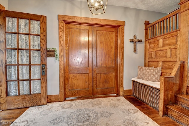 foyer entrance featuring an inviting chandelier, a textured ceiling, and dark hardwood / wood-style floors