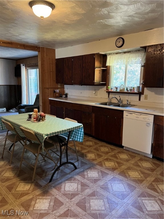 kitchen featuring sink, white dishwasher, dark parquet flooring, dark brown cabinetry, and wooden walls