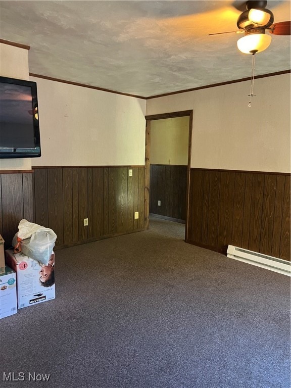 carpeted spare room with baseboard heating, ceiling fan, and wood walls