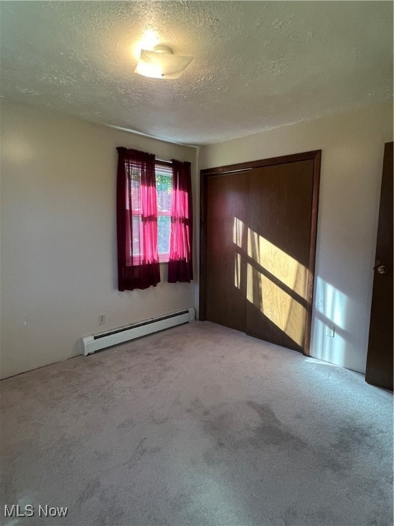 carpeted empty room featuring a textured ceiling and a baseboard heating unit