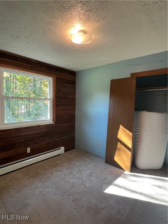 carpeted empty room with wood walls, a textured ceiling, and a baseboard heating unit