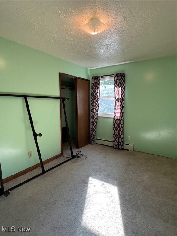 unfurnished bedroom featuring baseboard heating, a textured ceiling, light colored carpet, and a closet