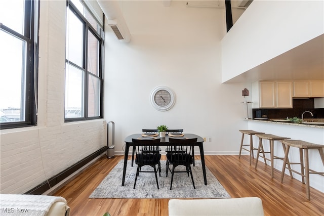 dining space featuring light wood-type flooring, a towering ceiling, brick wall, and sink