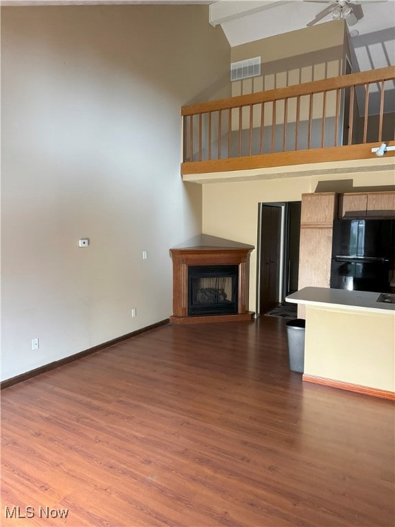 unfurnished living room with ceiling fan, a towering ceiling, and dark wood-type flooring