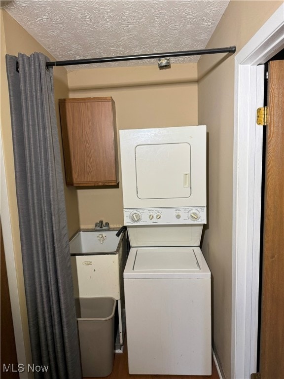 clothes washing area with stacked washer and dryer and a textured ceiling