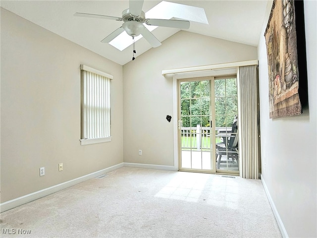 spare room with ceiling fan, light colored carpet, and vaulted ceiling with skylight