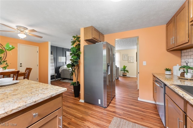 kitchen with a textured ceiling, tasteful backsplash, light hardwood / wood-style flooring, appliances with stainless steel finishes, and ceiling fan