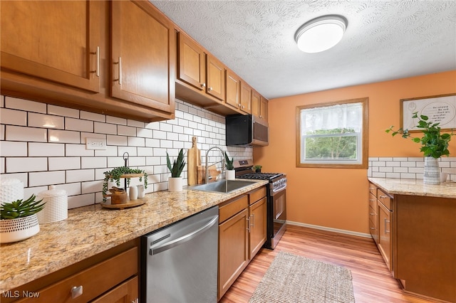 kitchen featuring appliances with stainless steel finishes, light hardwood / wood-style floors, light stone counters, a textured ceiling, and sink