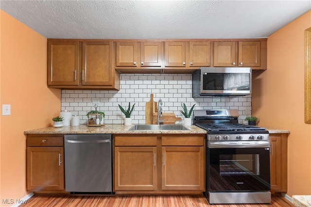 kitchen with light hardwood / wood-style floors, appliances with stainless steel finishes, sink, and decorative backsplash